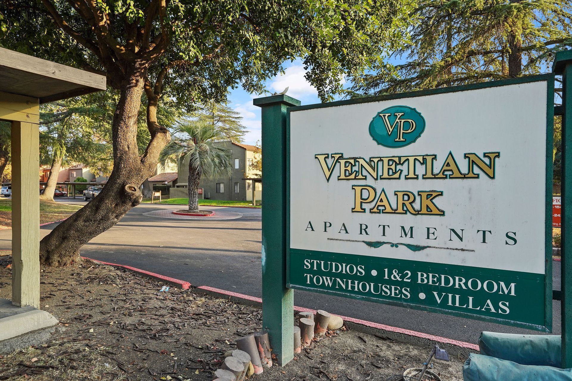 Venetian Park Apartments sign beside a tree and street in a sunny outdoor setting