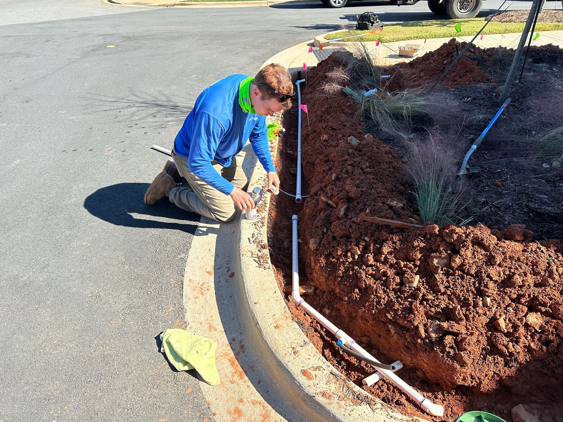 Man kneeling, working on irrigation pipes next to a curb and flower bed.
