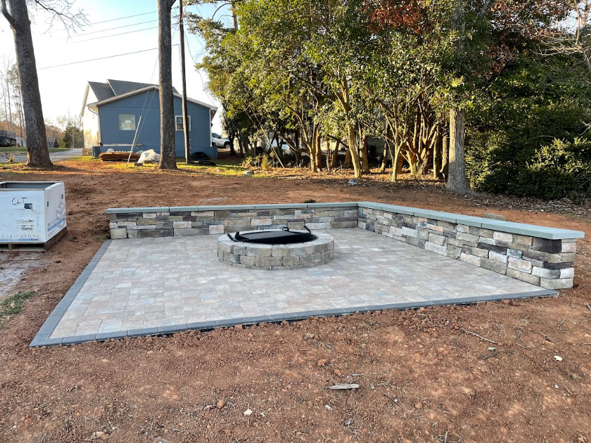 A brick patio with a fire pit, surrounded by a low brick wall, in a yard.