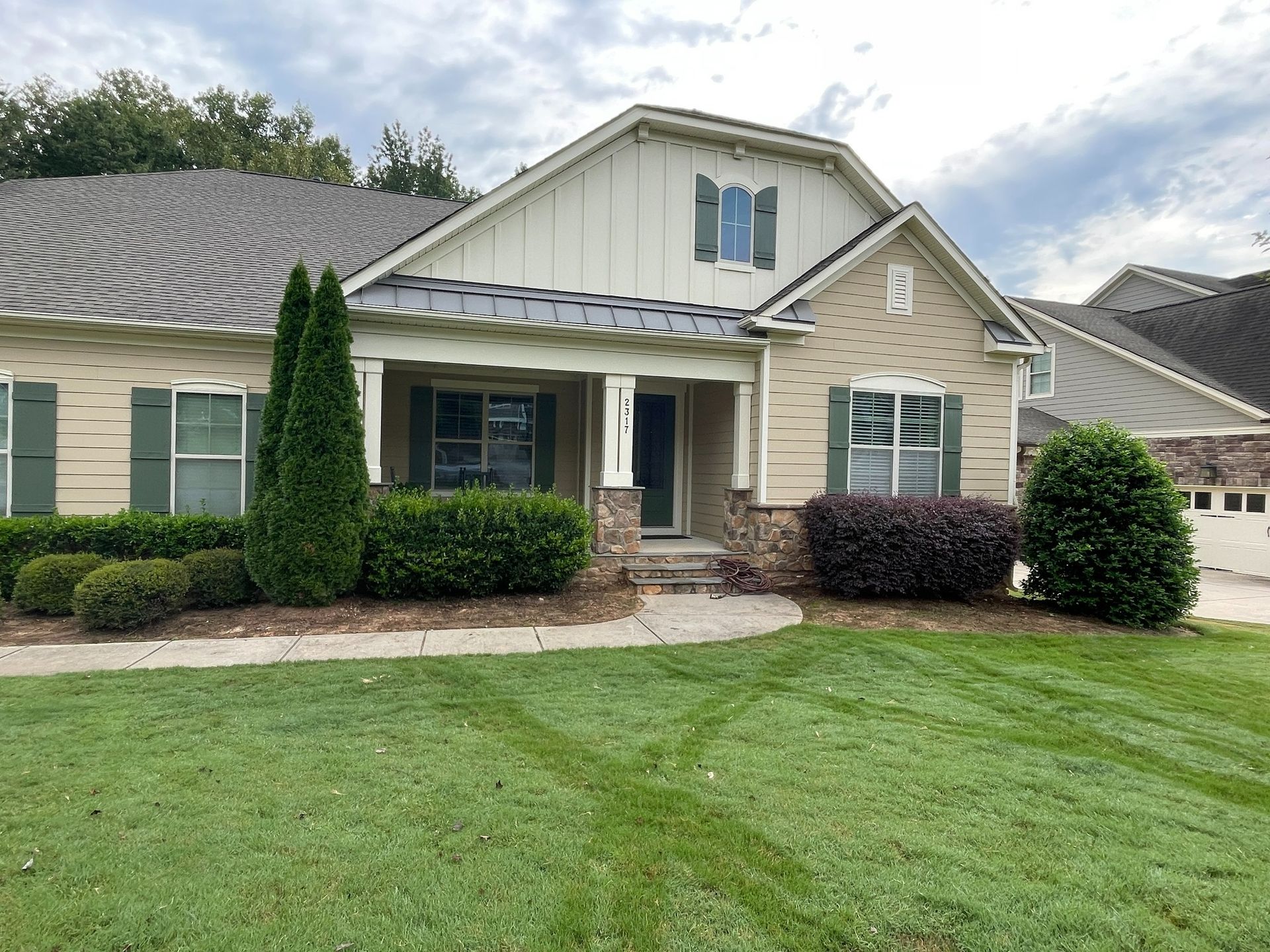 Suburban house with beige siding, green shutters, and well-manicured lawn.