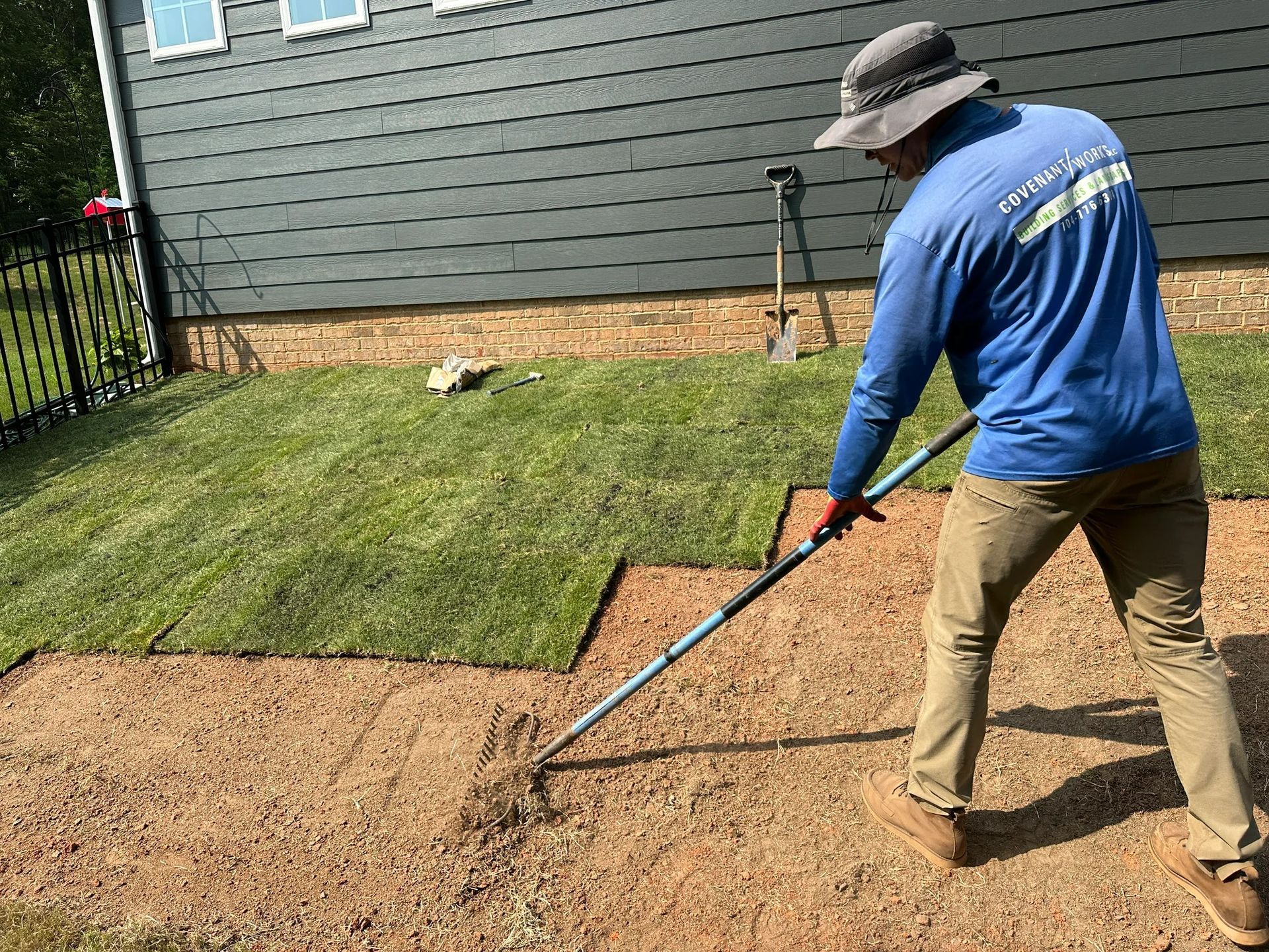 Man laying sod with a rake in a yard near a house.