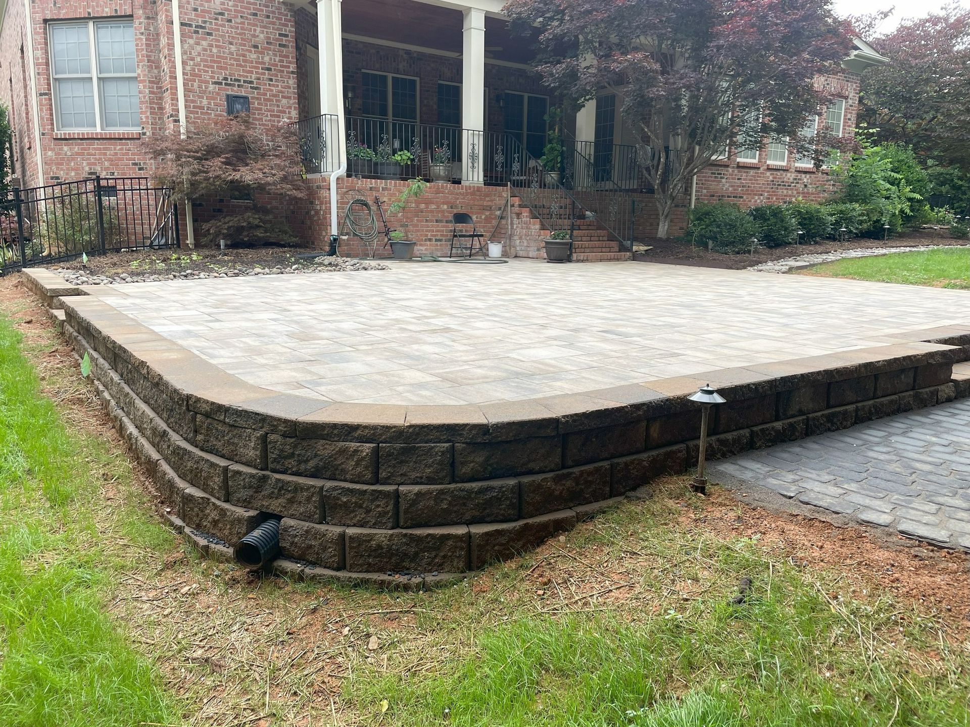 Stone patio with a low retaining wall, adjacent to a brick house and grass lawn.