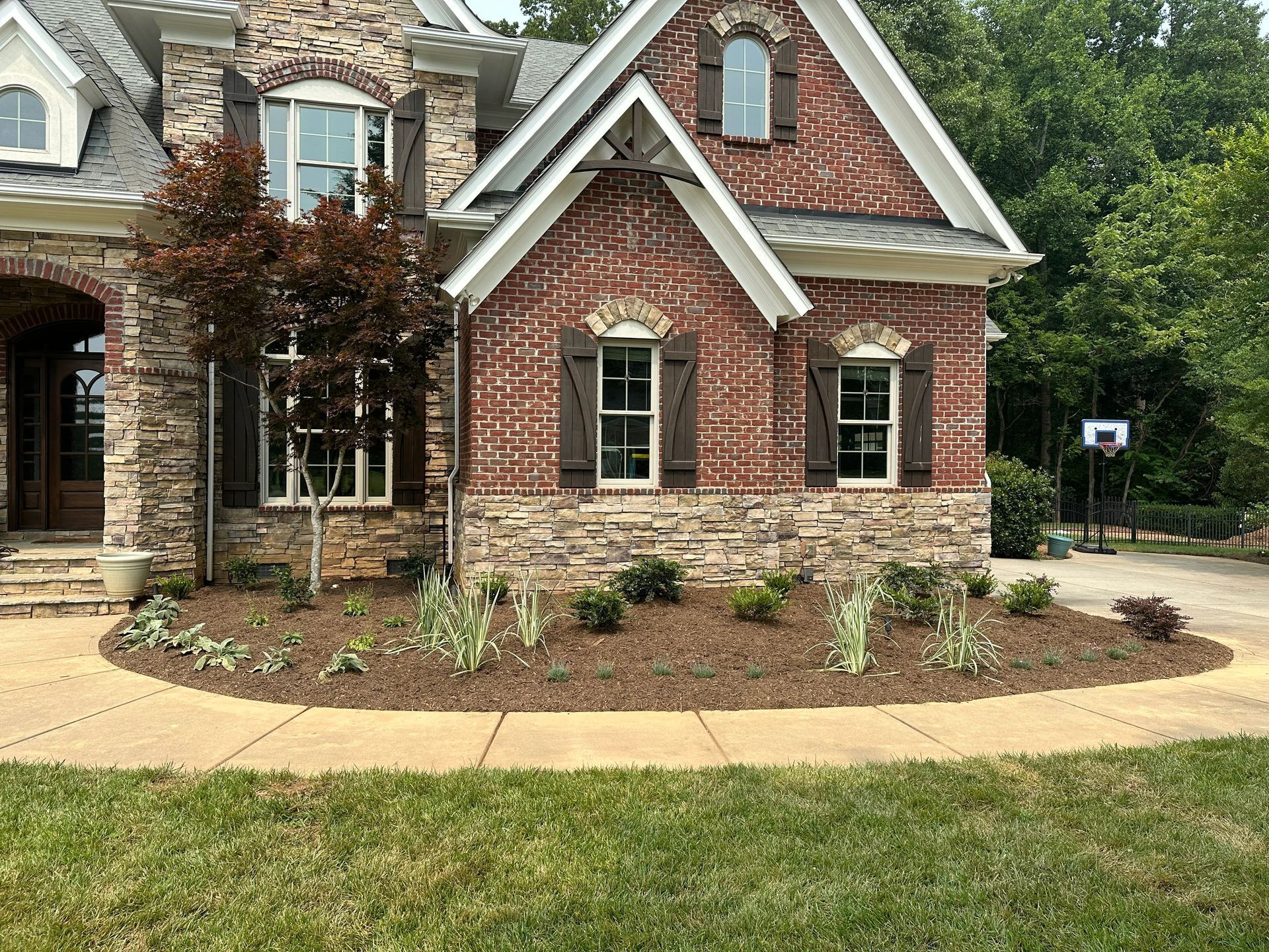 Brick house with stone base, landscaped yard, sidewalk, and green grass.