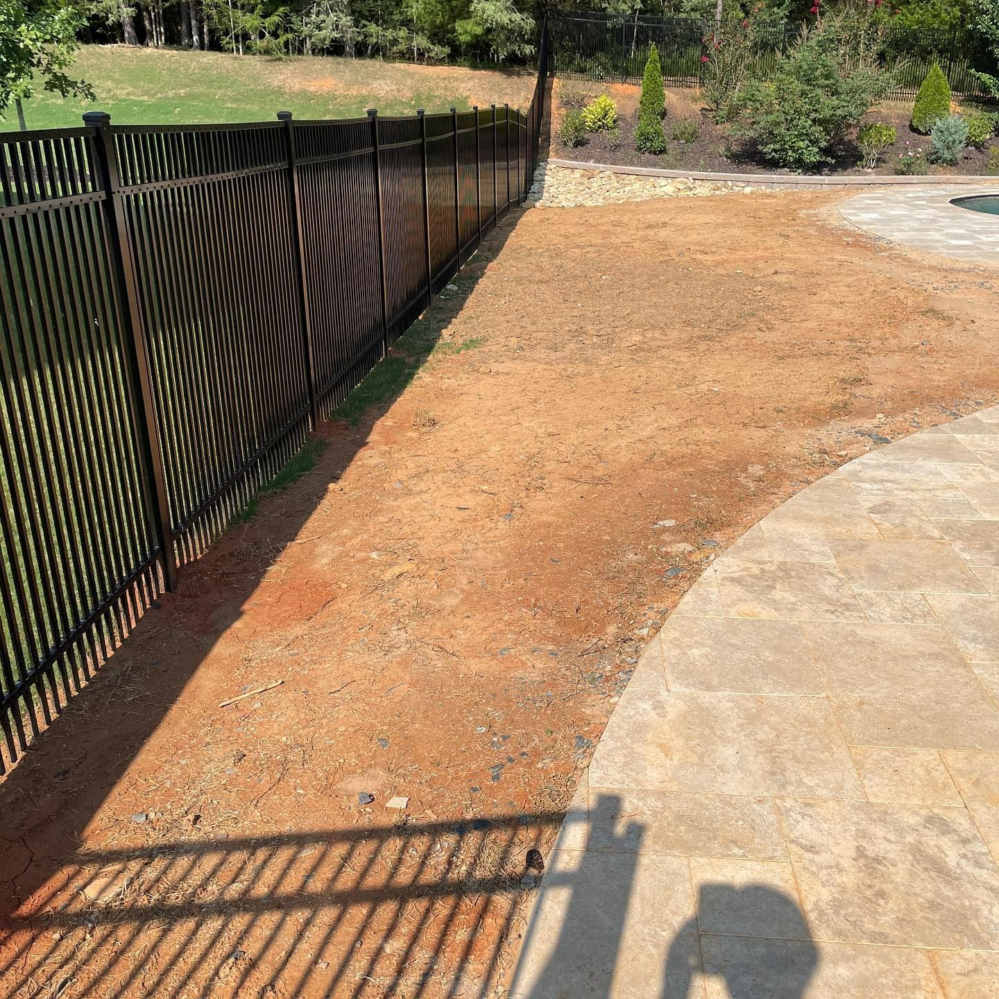 Black metal fence bordering dirt patch and concrete patio.