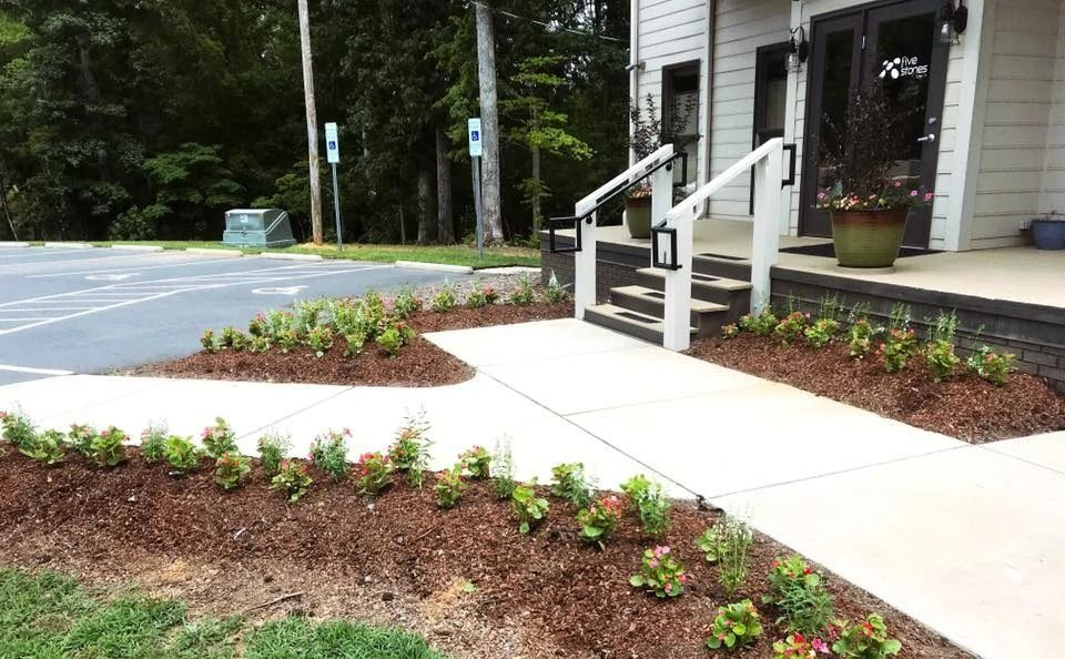 A building entrance with a sidewalk and landscaped flowerbeds.