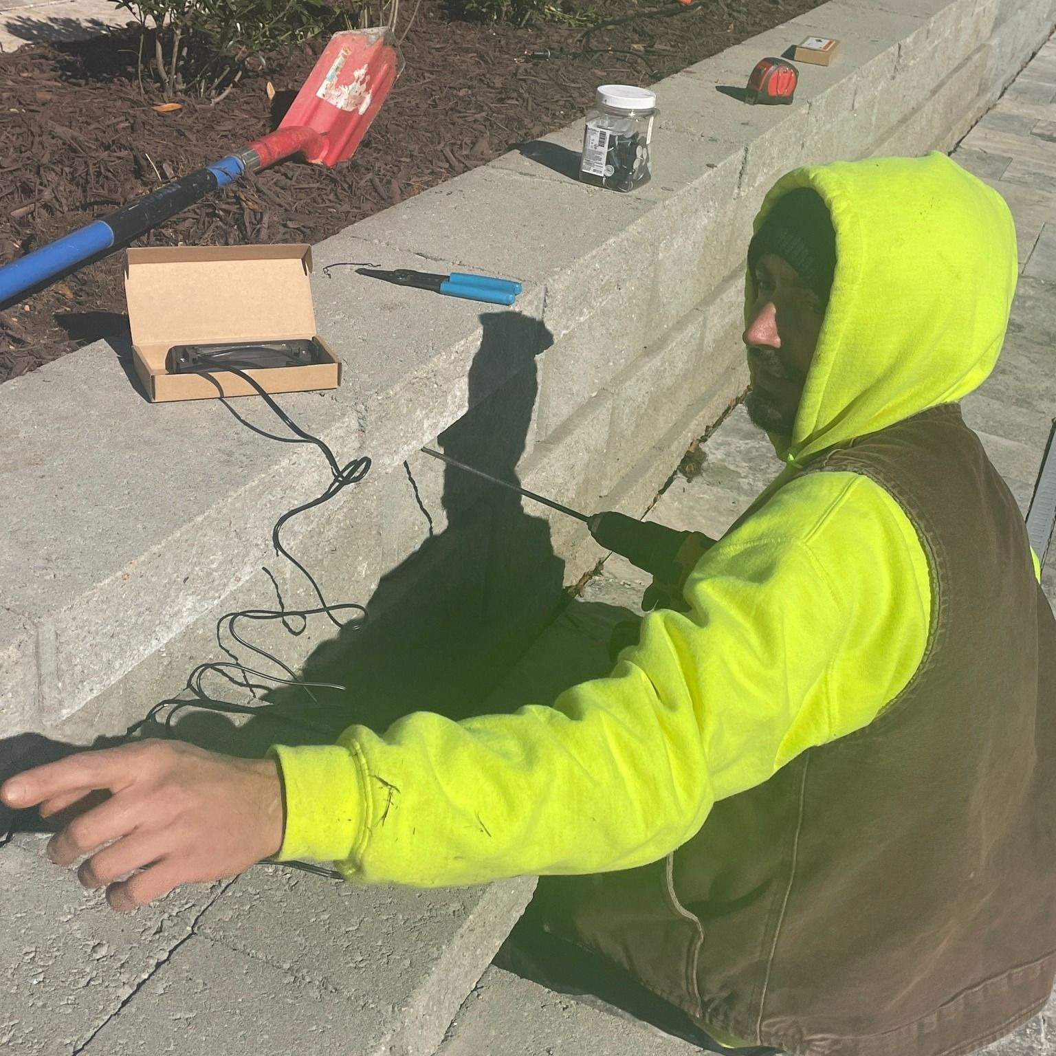Person in yellow hoodie working on a concrete structure with tools nearby.