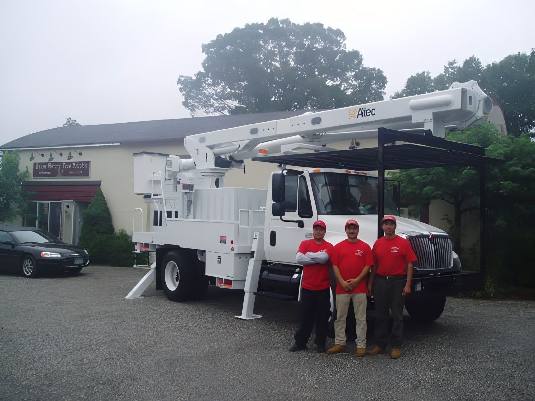 Three men in red shirts stand by a white bucket truck in front of a building.