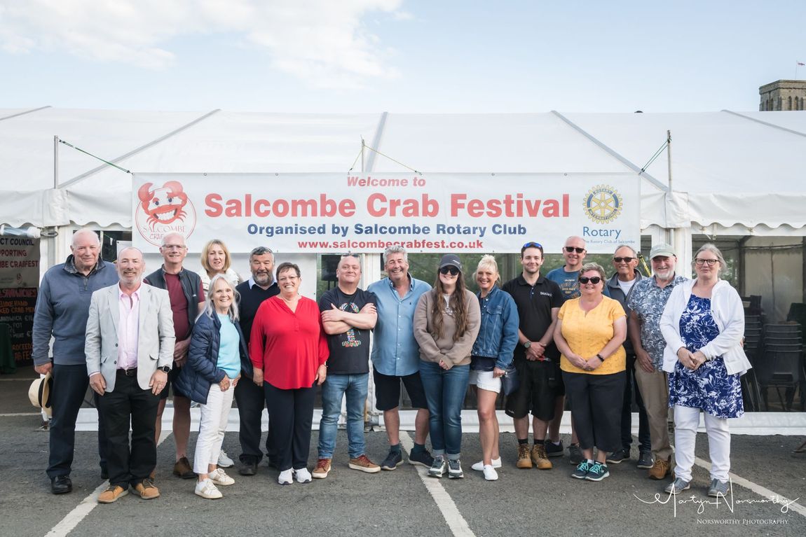 Five people smiling, arms around each other, at an outdoor bar with bottles and drinks.