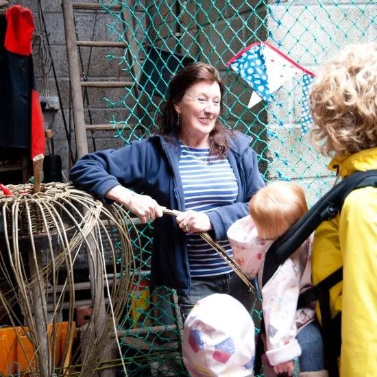 Woman in blue smiling near a fishing cage, interacting with people; net background.
