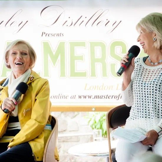 Two women smiling, holding microphones; one in yellow jacket, other in white, at 