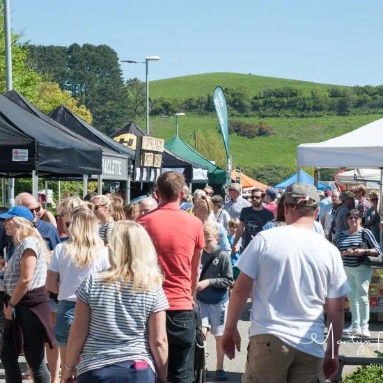 Crowd at outdoor market with tents and green hill in background.