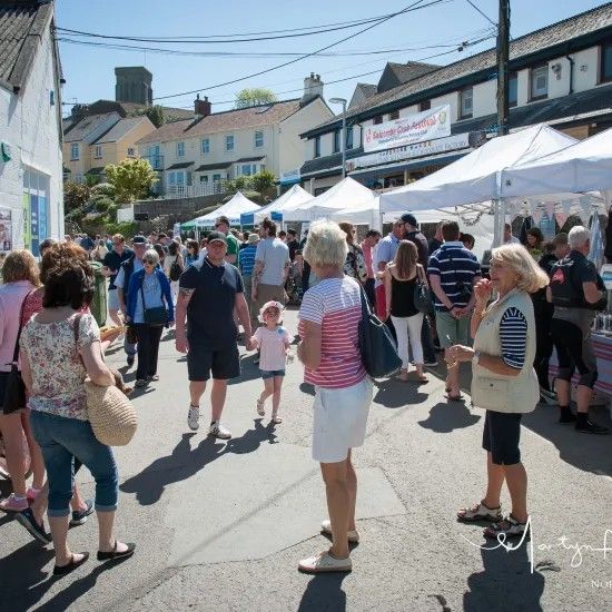 Street fair with white tents, crowds, and buildings under a sunny sky.