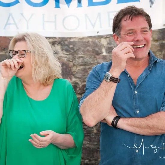 Woman in green laughs with man in blue shirt; both outdoors.