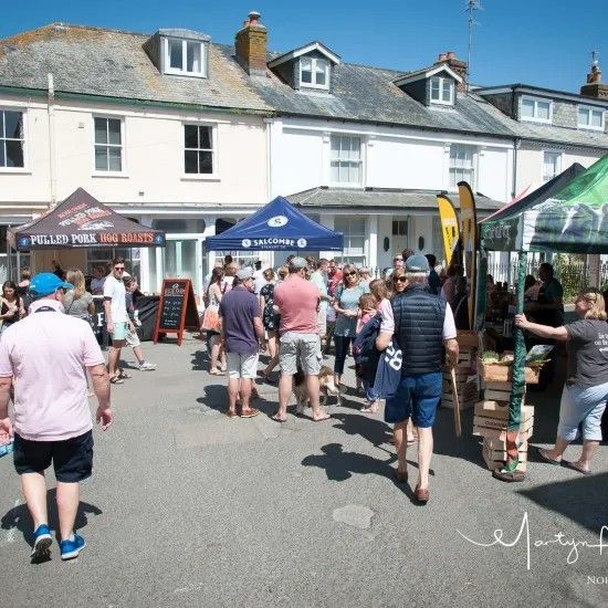 Outdoor market with people browsing stalls, sunny day.