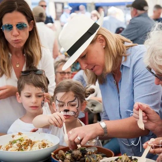 Woman serves food to children with painted faces at outdoor event.