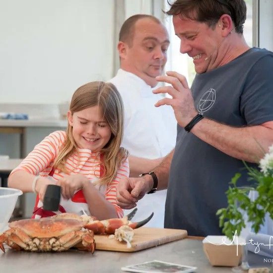 Girl cracking crab with mallet, man and chef watch, kitchen setting.
