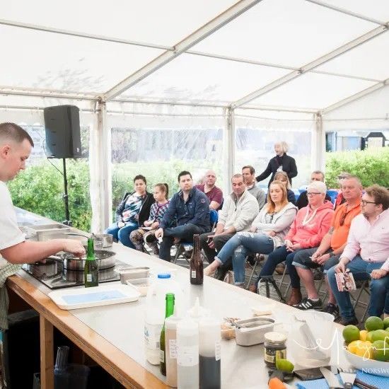 Chef demonstrates cooking techniques to an audience seated in a tent.