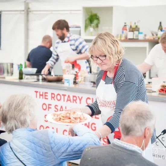 Woman serving food at a Rotary Club event. Others cook behind the counter.