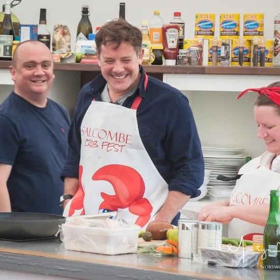 Three people smiling in a kitchen setting; one wearing a 