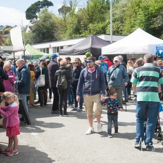 Crowd at an outdoor market with white tents, sunny day. People shopping, child holding an adult's hand.
