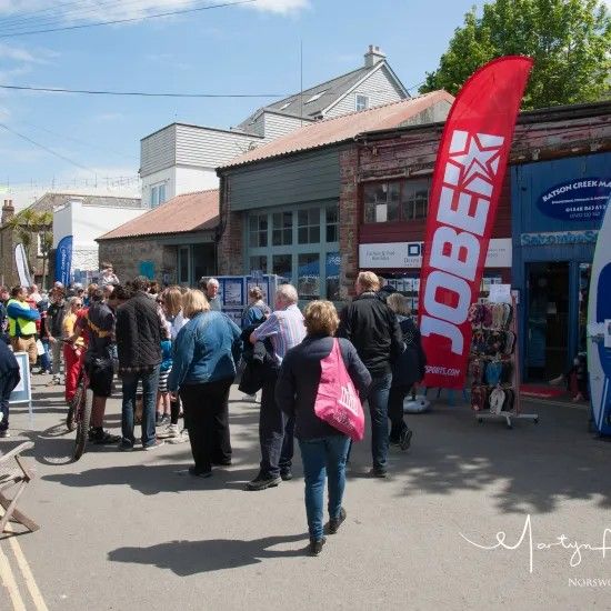 Crowd gathered outside shops, red Jobe flag, sunny day.