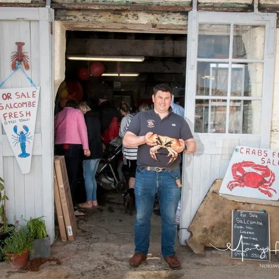 Man holding crab in a doorway of a seafood shop; signs for lobster & crabs on the wall.