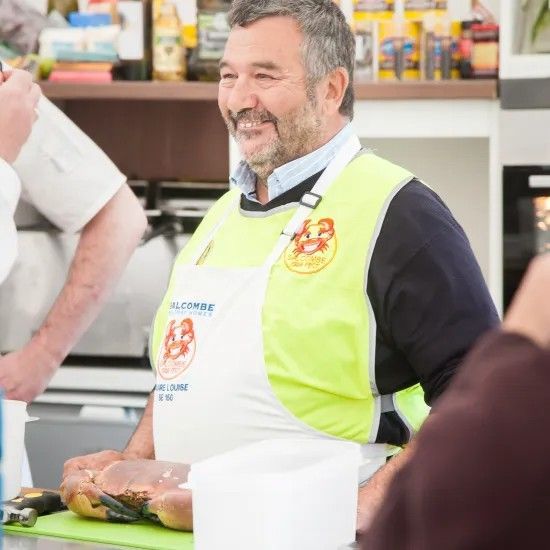 Man in apron smiles, preparing seafood at a counter.