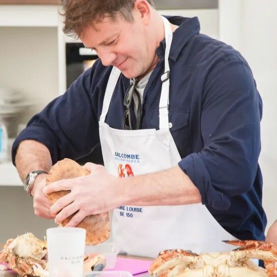 Man in apron cracking open a crab indoors; kitchen setting.