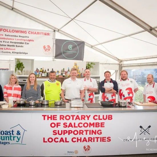Group of people cooking at an event under a tent, supporting local charities.
