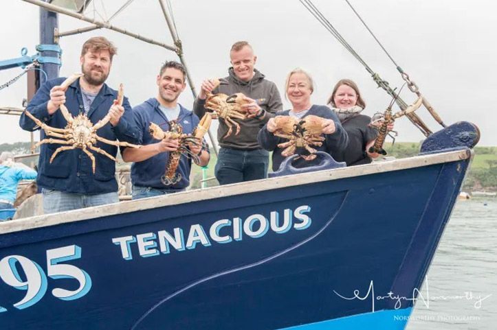 Five people on a boat, holding up crabs and lobsters. 