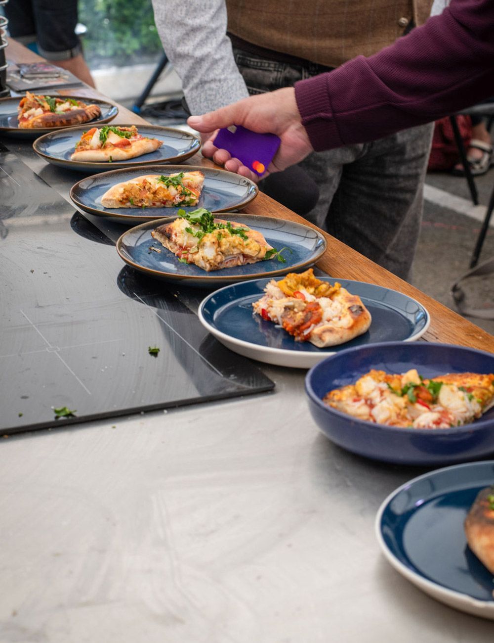 Plates of food lined up on a surface, being assessed. A person holds a purple device over them.