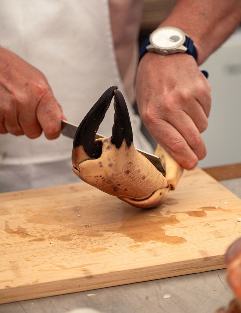 Chef cutting open a crab claw on a wooden cutting board with a knife.