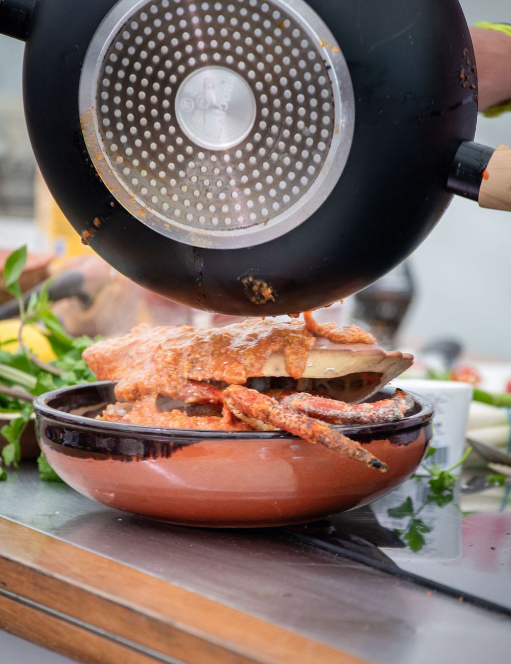Crab in a bowl being drizzled with sauce from a black pan.