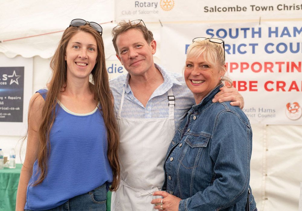 Three people smiling together at an outdoor event, with white tent in background.