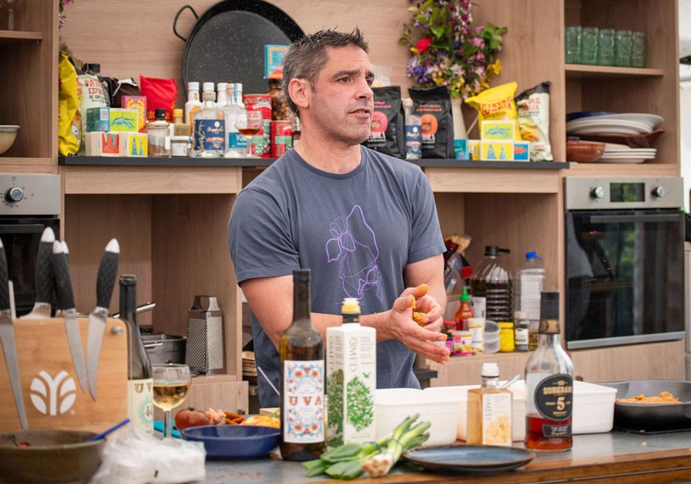 Man in a kitchen, holding food. Kitchen counter with ingredients, bottles, and a baking oven.