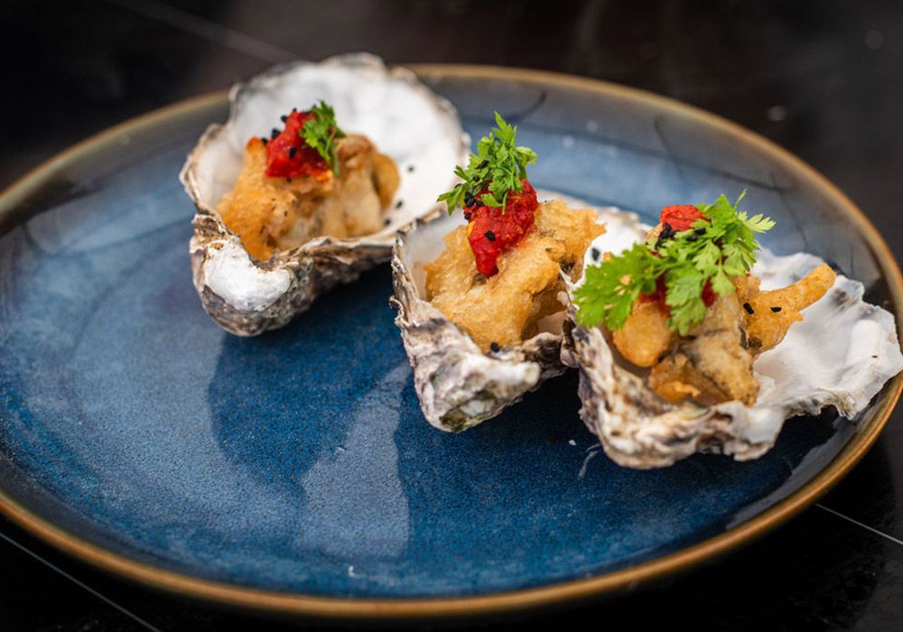 Three fried oysters with red garnish and cilantro on a blue plate.