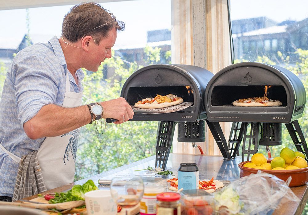 Man cooking pizza in outdoor ovens, kitchen setting.