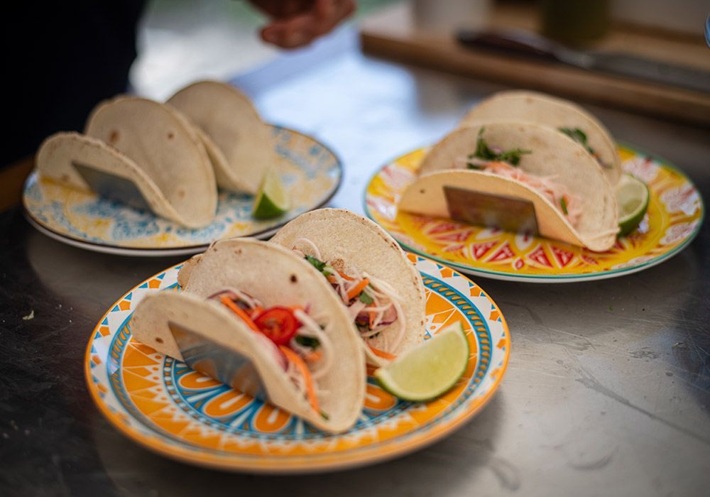 Tacos on colorful plates, with lime wedges. Two filled with toppings, one with empty shells.