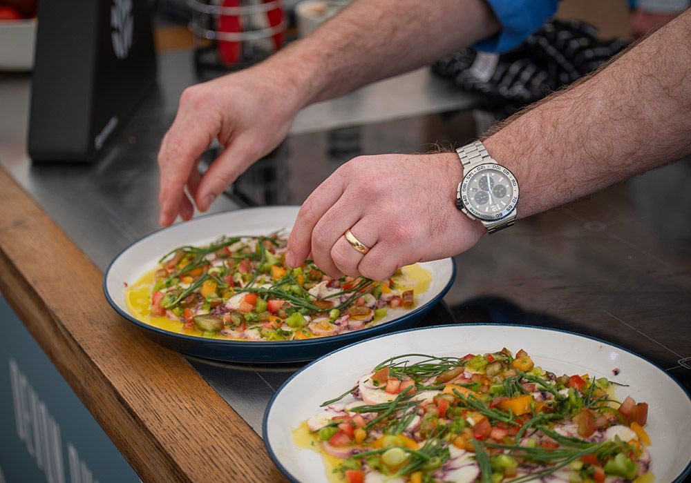 Hands plating food onto two dishes with colorful toppings.