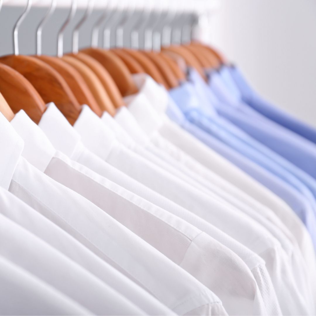 A row of shirts hanging on wooden hangers in a closet.