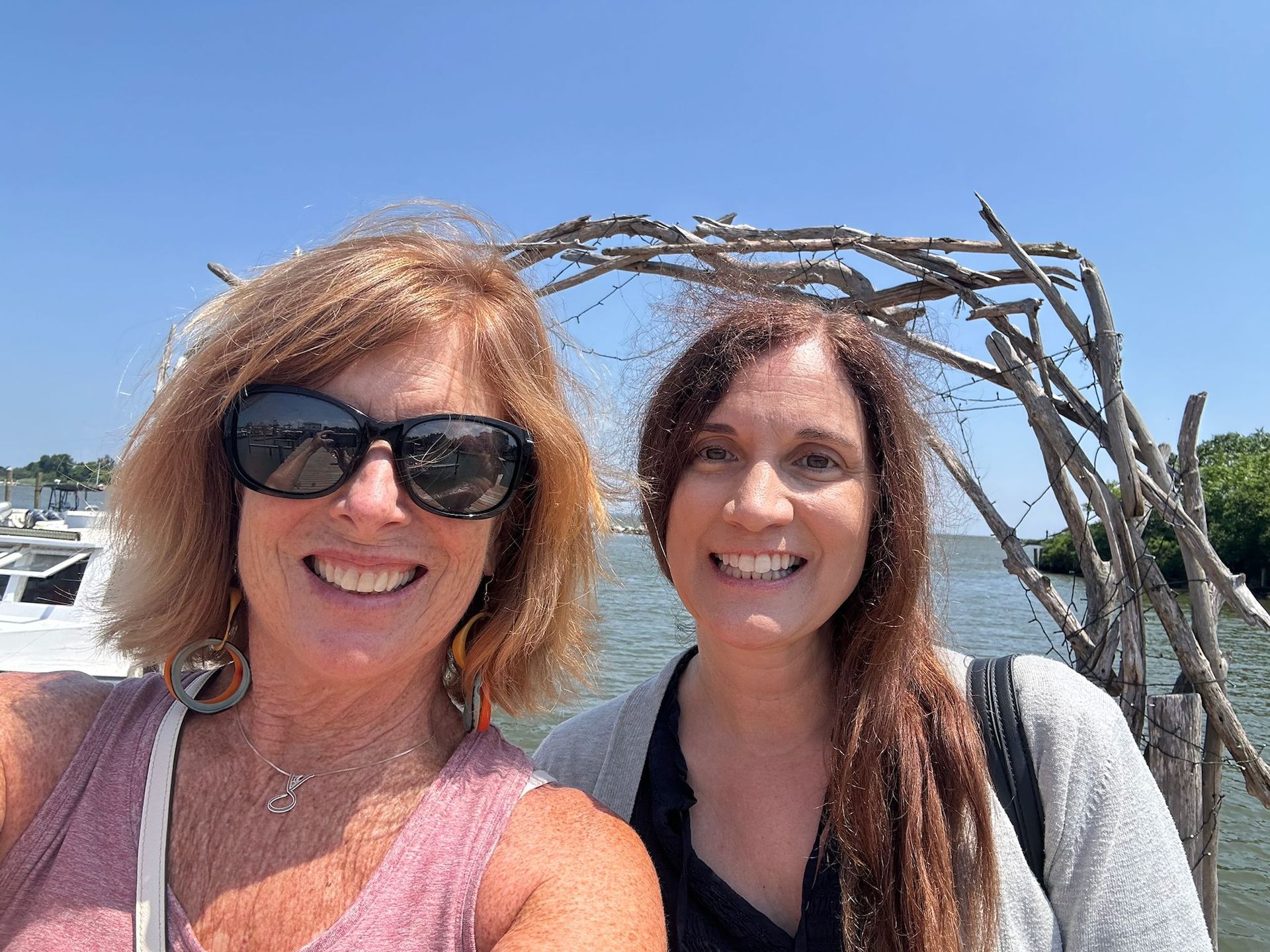 Two women wearing sunglasses are standing next to each other in front of a body of water.
