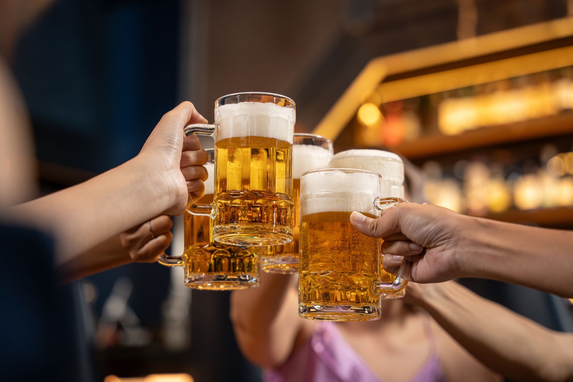 A group of people are toasting with beer mugs in a bar.