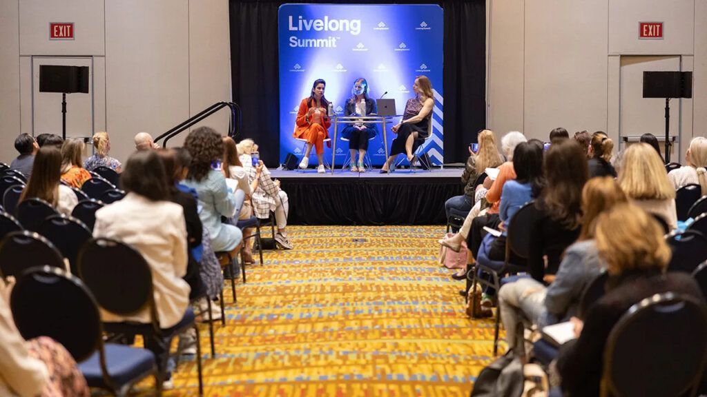 A group of people are sitting in chairs in front of a stage at a conference.