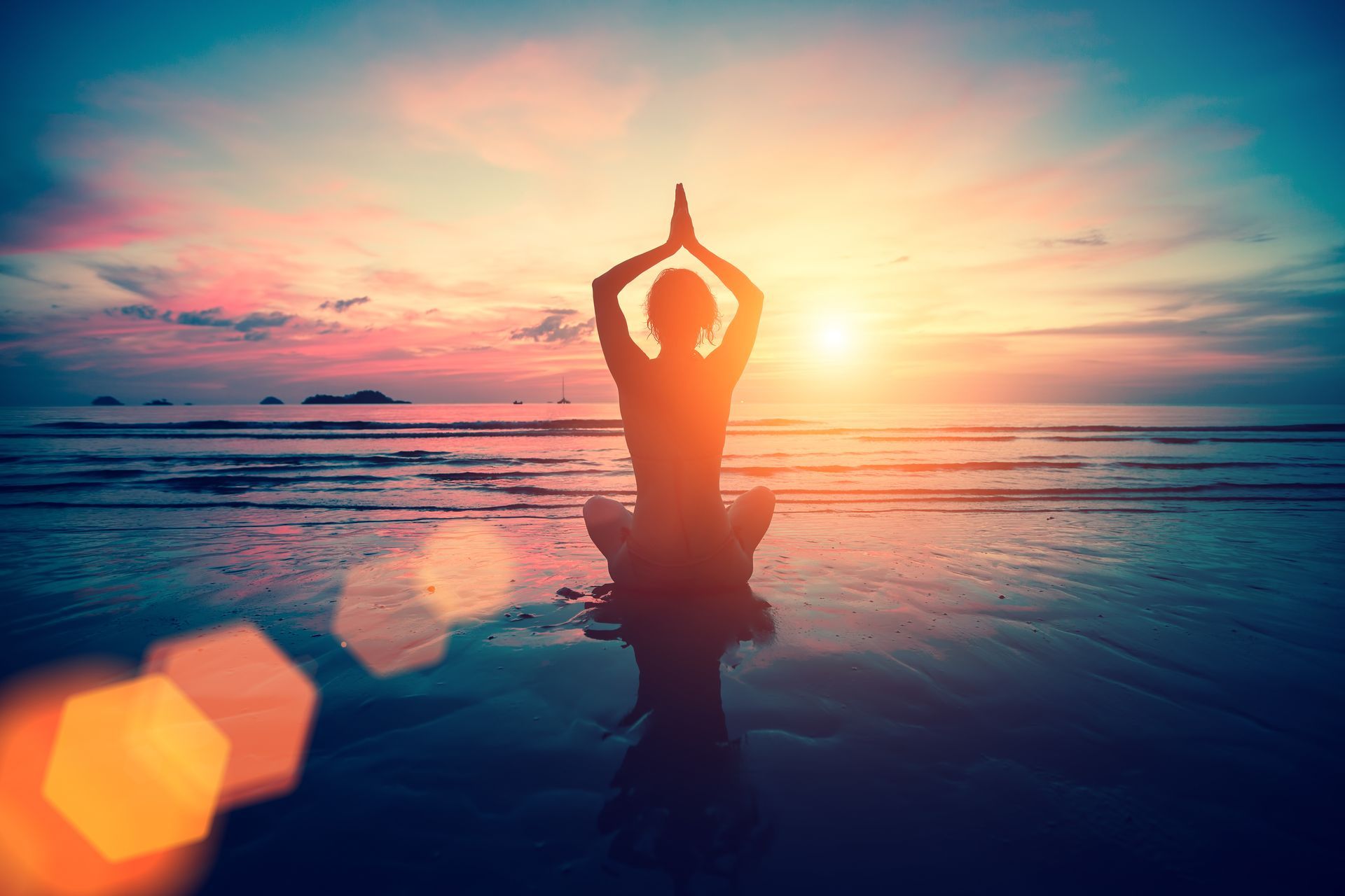 A woman is practicing yoga on the beach at sunset.