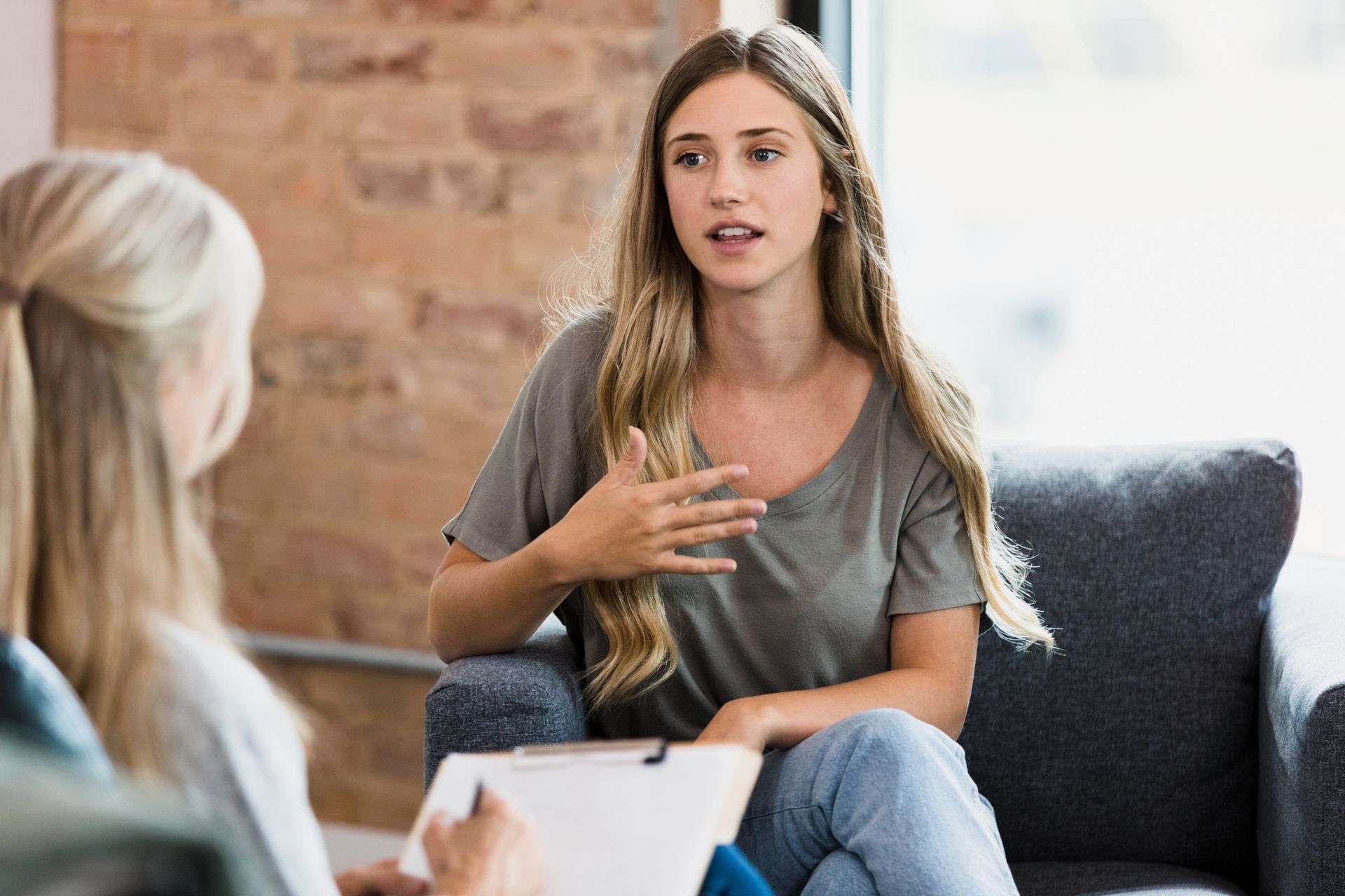 Woman in gray shirt gestures while talking in therapy session.