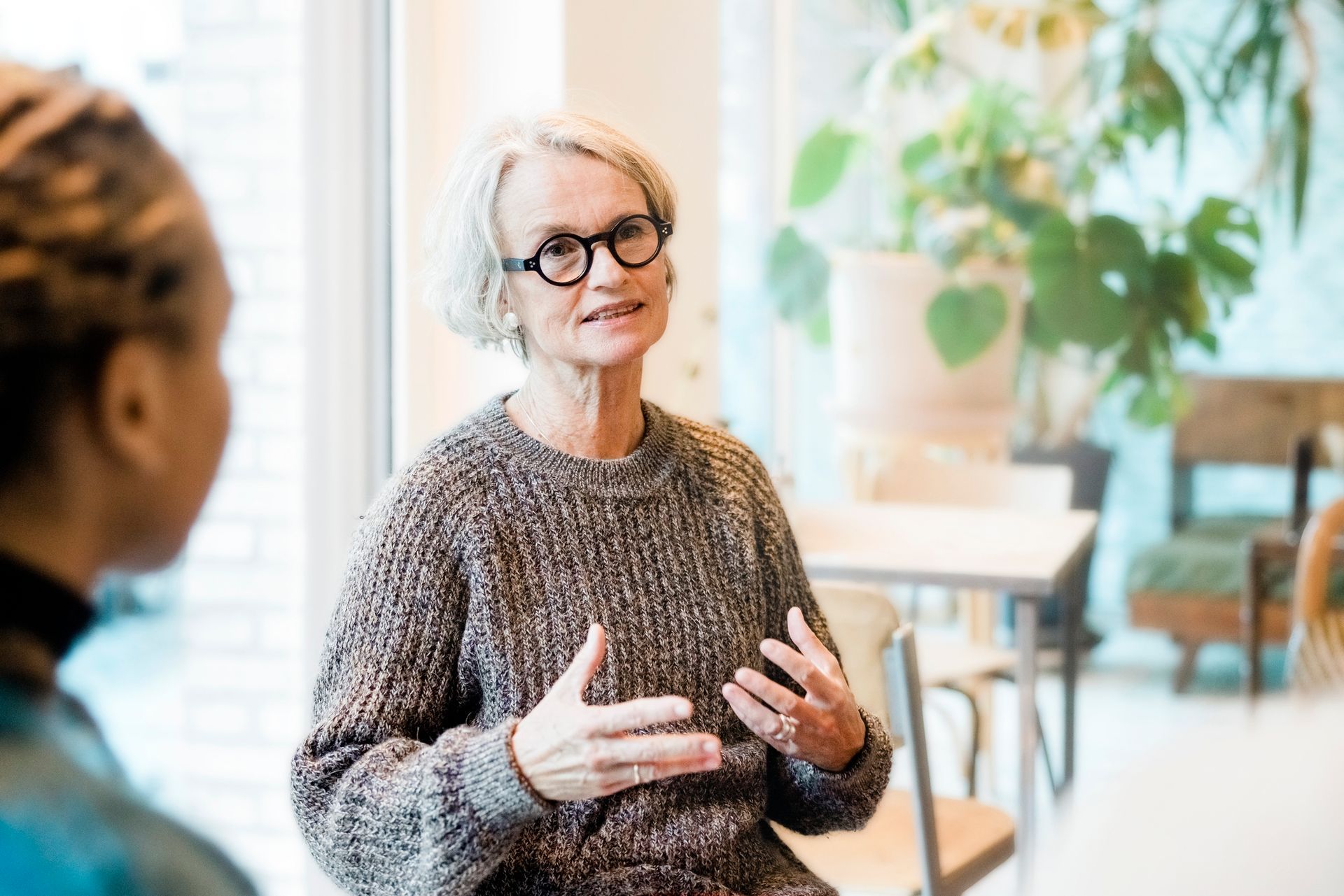 Woman in glasses gesturing while talking, possibly in a meeting.