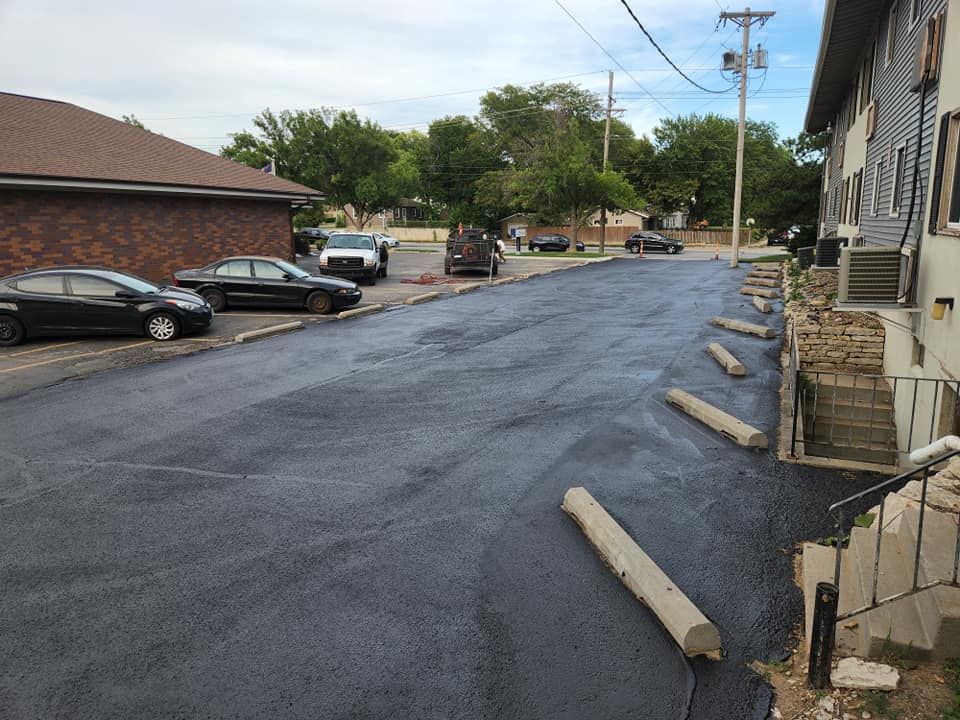 Newly paved asphalt driveway with parked cars and concrete parking stops.