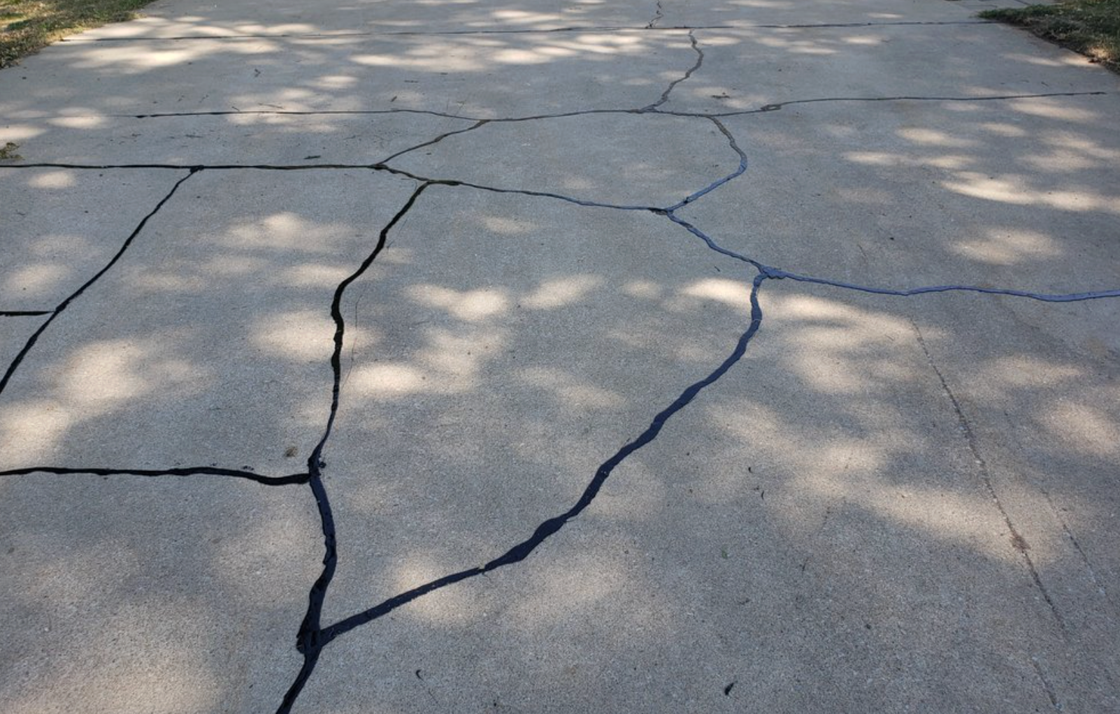 A gray concrete surface with multiple deep cracks that have been filled with black sealant.