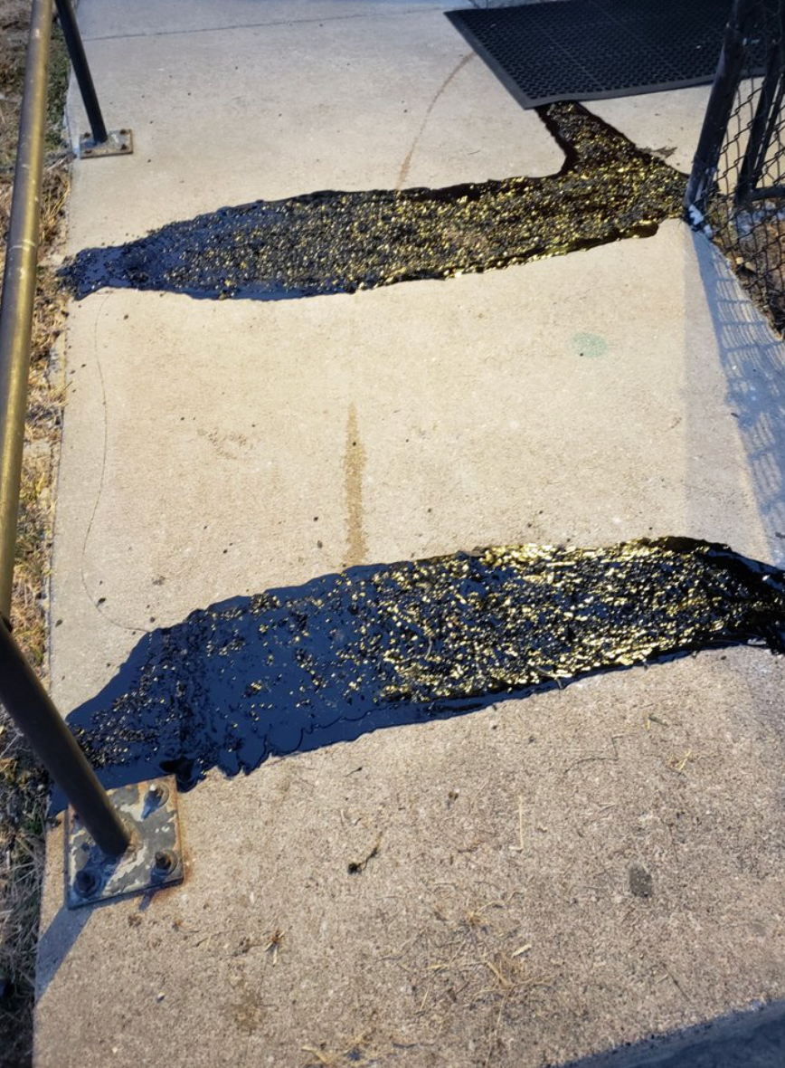 Two large, black asphalt patches applied across a concrete sidewalk, appearing wet and uneven.