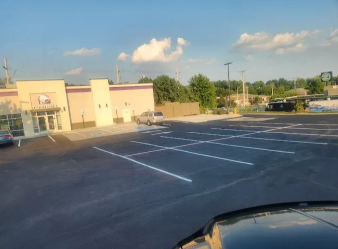 A Taco Bell restaurant with a parking lot in front, seen from the perspective of someone inside a vehicle.
